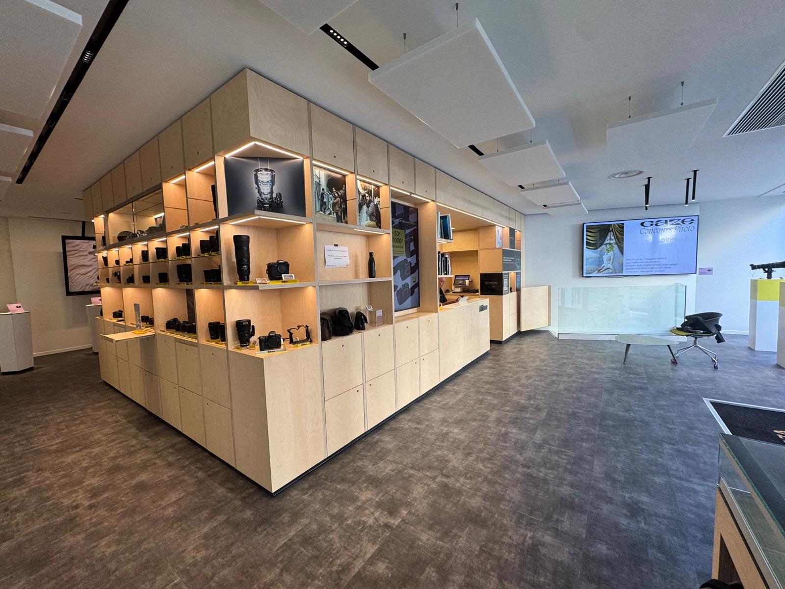 Wide view of the Nikon Pro showroom: display island, back-lit shelving and acoustic ceiling.