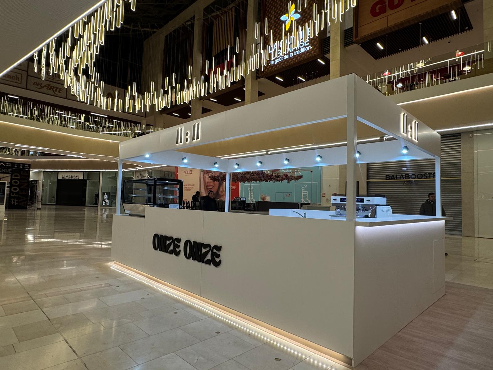 Onze Onze kiosk at night: illuminated 11:11 canopy and warm LED counter.